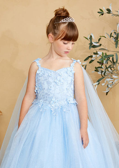Young girl in a light blue gown standing indoors with a neutral background