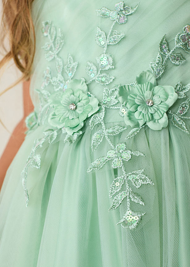 Crafted for the discerning eye, this floor-length girls sage green gown showcases a beautifully pleated bodice embellished with dimensional floral lace and shimmering iridescent accents